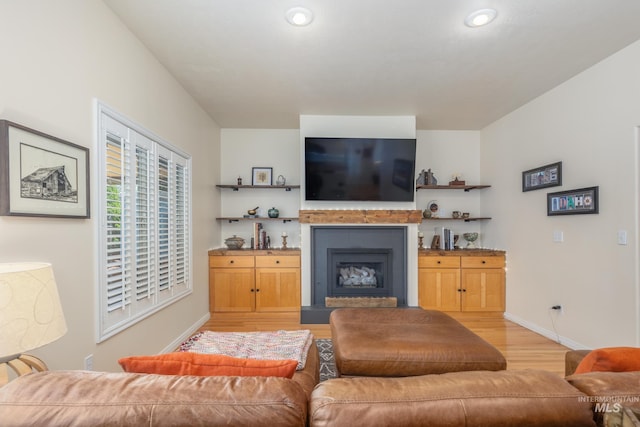 living area featuring a fireplace with raised hearth, baseboards, recessed lighting, and light wood-style floors