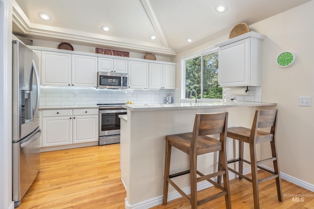 kitchen featuring a peninsula, appliances with stainless steel finishes, a breakfast bar, and tasteful backsplash