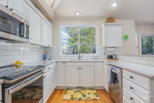 kitchen with a sink, white cabinets, stainless steel appliances, and light wood-type flooring