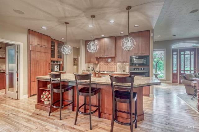 705 N Cobblestone Way, Eagle, ID 83616 - kitchen featuring black appliances, light wood-type flooring, a large island, tasteful backsplash, and baseboards