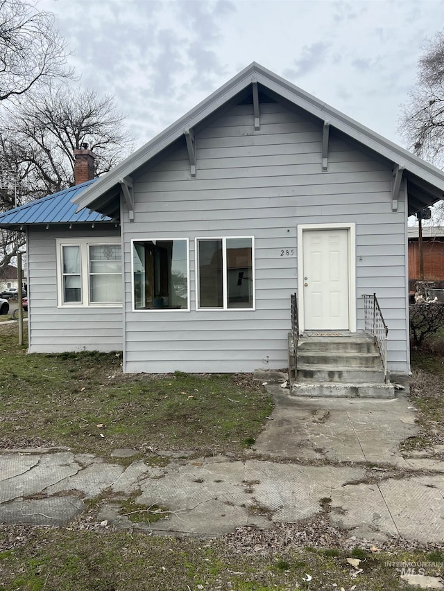 bungalow-style home featuring entry steps, metal roof, and a chimney