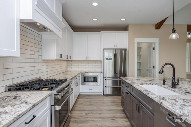 kitchen with high end appliances, white cabinets, sink, pendant lighting, and premium range hood