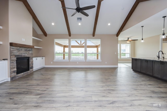 unfurnished living room featuring light hardwood / wood-style floors, a stone fireplace, beam ceiling, and sink