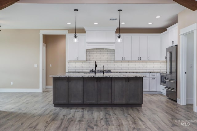 kitchen featuring white cabinets, light wood-type flooring, hanging light fixtures, and a center island with sink