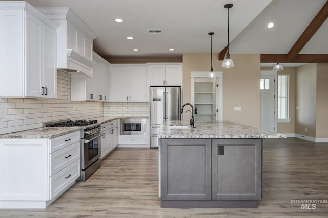 kitchen with an island with sink, premium appliances, white cabinetry, and light hardwood / wood-style flooring