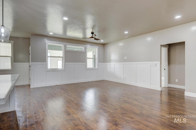 1113 W Blaine Ave, Nampa, ID 83651 - unfurnished living room featuring a decorative wall, ceiling fan, visible vents, a wainscoted wall, and dark wood-style flooring