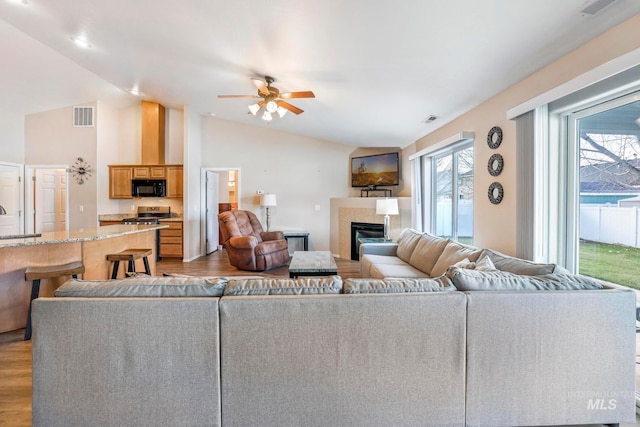 living room with a tile fireplace, light hardwood / wood-style floors, vaulted ceiling, and ceiling fan