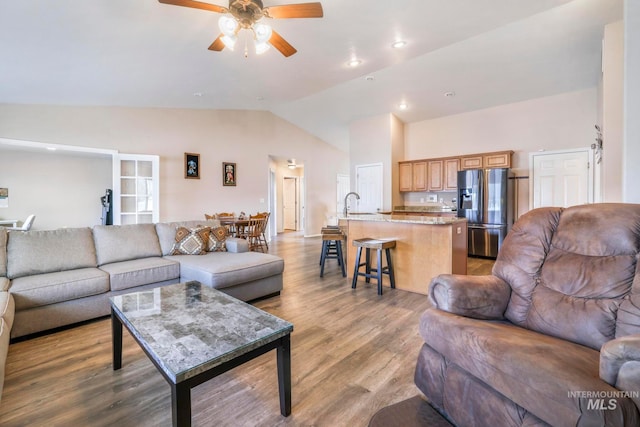 living room featuring ceiling fan, lofted ceiling, sink, and light hardwood / wood-style flooring