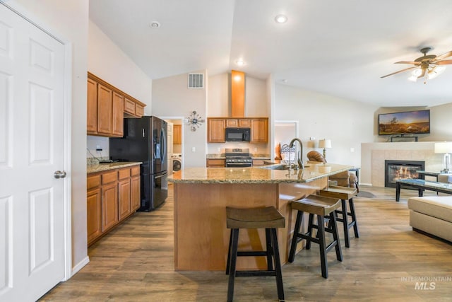 kitchen with a breakfast bar, a kitchen island with sink, black appliances, a tile fireplace, and hardwood / wood-style floors