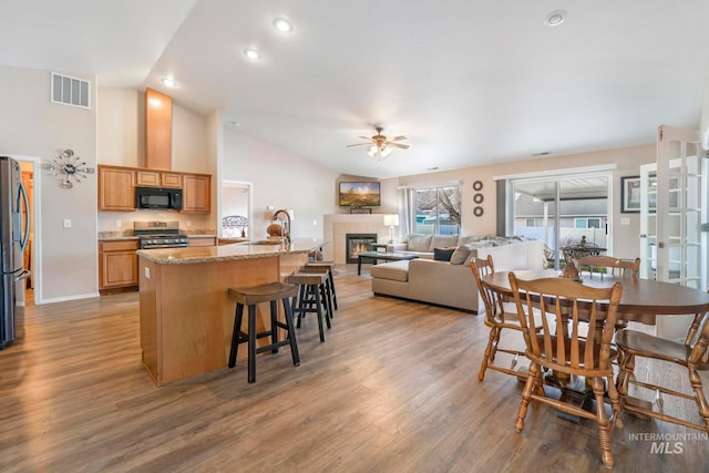 dining area featuring vaulted ceiling, ceiling fan, sink, a tile fireplace, and hardwood / wood-style floors