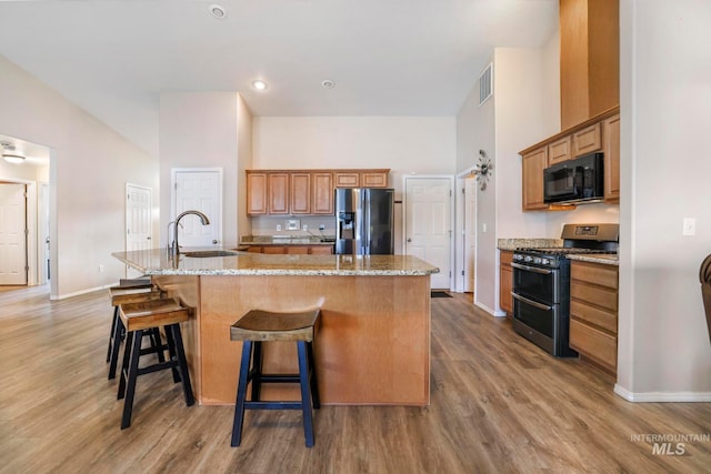 kitchen with a center island with sink, a kitchen breakfast bar, sink, light stone counters, and stainless steel appliances