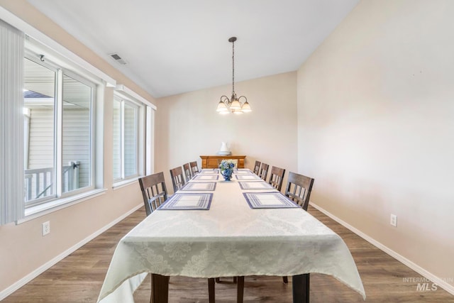 dining area featuring dark hardwood / wood-style flooring, lofted ceiling, and an inviting chandelier