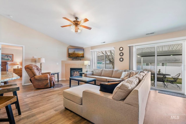 living room featuring ceiling fan, vaulted ceiling, light wood-type flooring, and a tiled fireplace