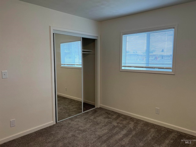 unfurnished bedroom with multiple windows, a closet, and dark colored carpet