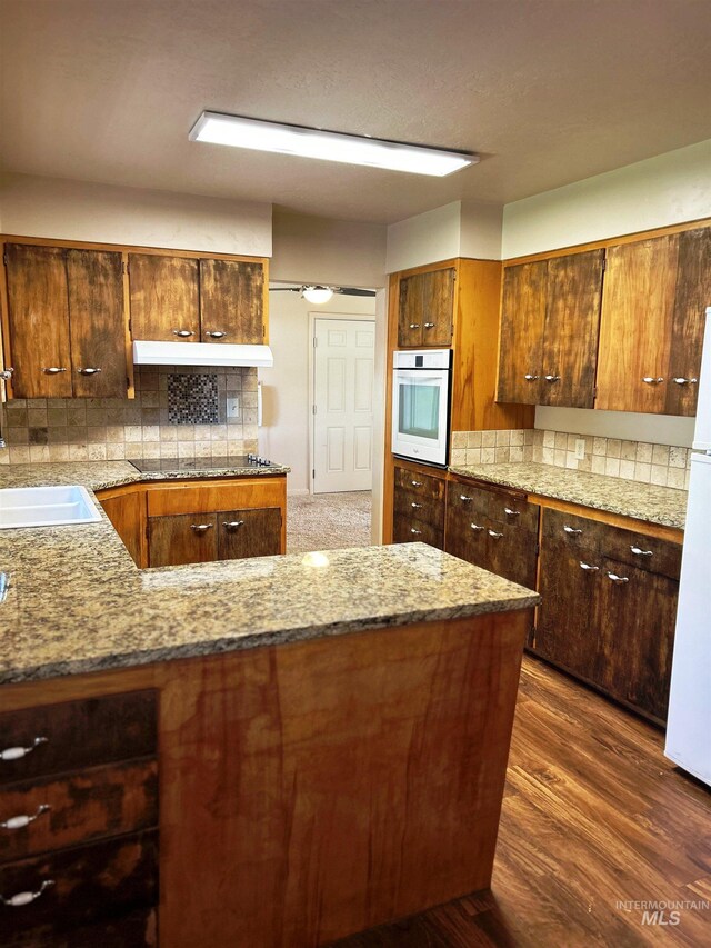 2320 S Illinois, Caldwell, ID 83605 - kitchen with white appliances, backsplash, light stone counters, dark wood-type flooring, and under cabinet range hood