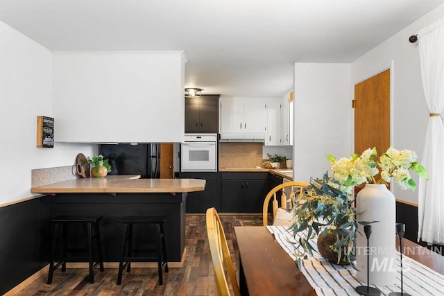 5928 W Grunder, Boise, ID 83709 - kitchen with white oven, freestanding refrigerator, under cabinet range hood, dark wood-style floors, and a peninsula