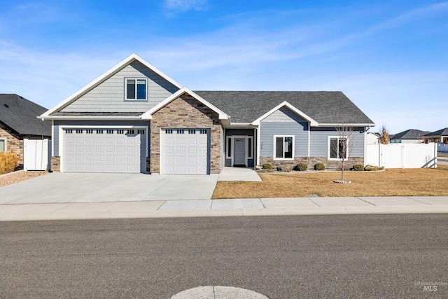 craftsman-style house with fence, roof with shingles, a front yard, stone siding, and driveway