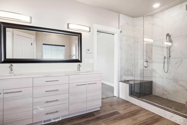 full bathroom with a sink, a marble finish shower, wood finished floors, and double vanity