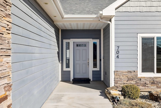 view of exterior entry with stone siding and roof with shingles