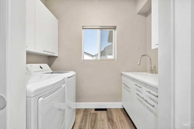 clothes washing area with light wood-style flooring, washer and clothes dryer, a sink, cabinet space, and baseboards