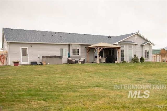 rear view of property with a gazebo, a hot tub, and a lawn