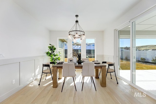 dining space with light wood-style floors, a notable chandelier, wainscoting, and a decorative wall