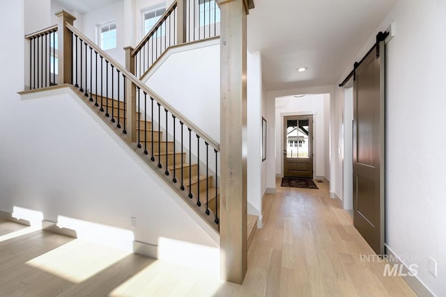 staircase featuring a wealth of natural light, a barn door, baseboards, and wood finished floors