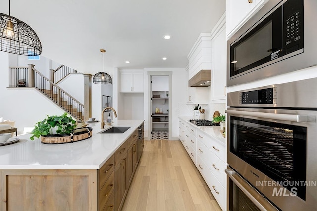 kitchen with light wood-type flooring, light countertops, white cabinets, stainless steel appliances, and a sink