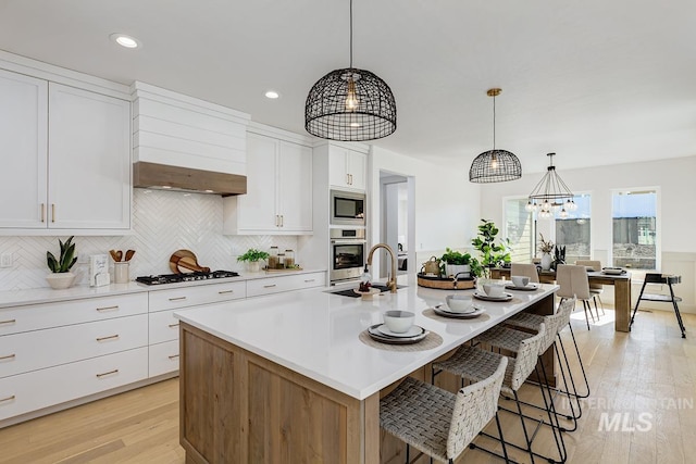 kitchen featuring light wood-type flooring, a center island with sink, appliances with stainless steel finishes, white cabinets, and light countertops