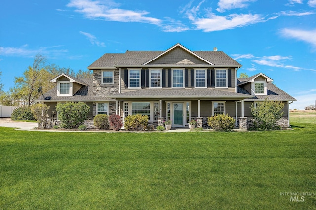 view of front of home with stone siding, a front yard, covered porch, and a shingled roof