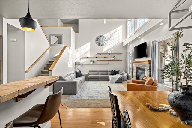 dining space featuring stairway, a high ceiling, a fireplace, a textured ceiling, and light wood-type flooring