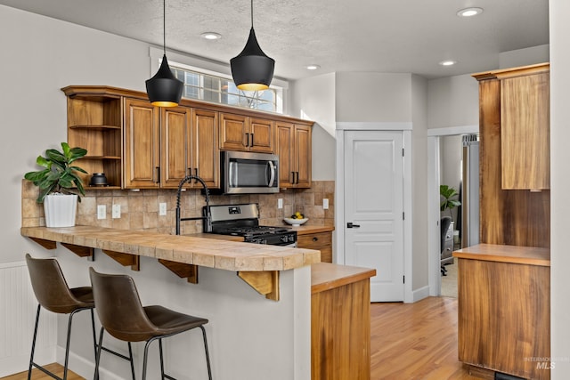 kitchen with light countertops, a peninsula, a kitchen breakfast bar, stainless steel appliances, and open shelves