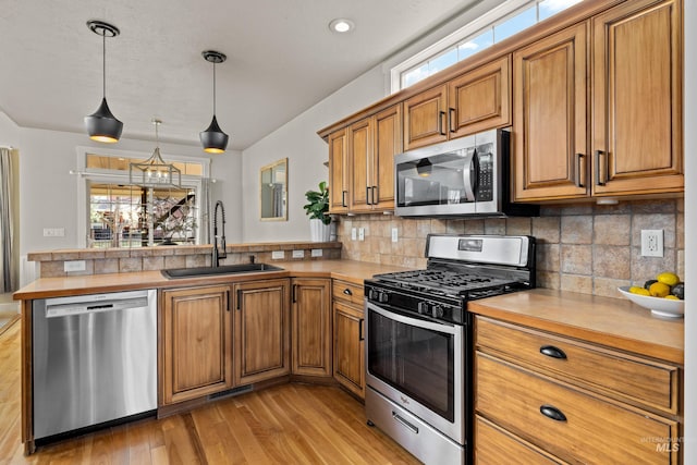 kitchen featuring brown cabinets, a sink, appliances with stainless steel finishes, a peninsula, and light countertops