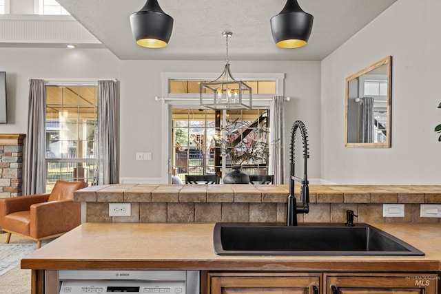 kitchen featuring dishwashing machine, a sink, pendant lighting, open floor plan, and a chandelier