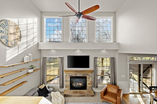 living room featuring a fireplace, a high ceiling, ceiling fan, and wood finished floors