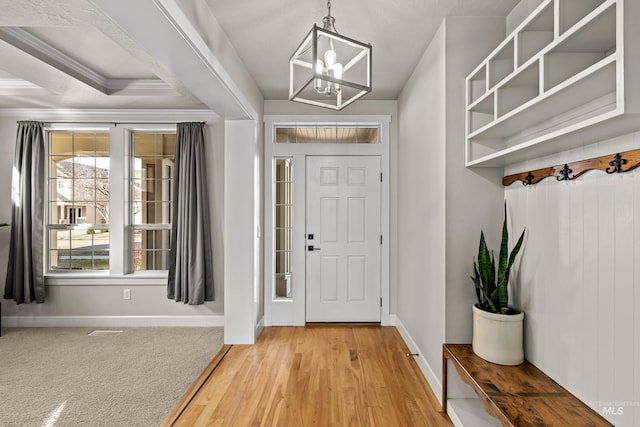 foyer entrance featuring crown molding, baseboards, light colored carpet, light wood-style flooring, and an inviting chandelier