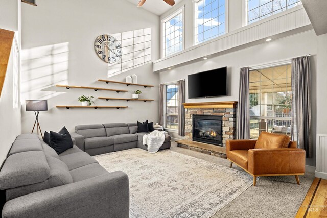 living room featuring a stone fireplace, wood finished floors, a ceiling fan, and a healthy amount of sunlight