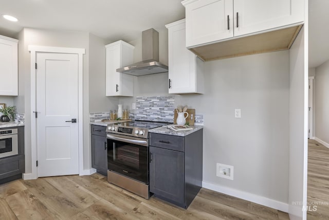 kitchen with light wood finished floors, tasteful backsplash, wall chimney exhaust hood, stainless steel appliances, and white cabinetry