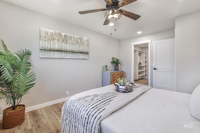 bedroom featuring recessed lighting, a spacious closet, ceiling fan, wood finished floors, and baseboards