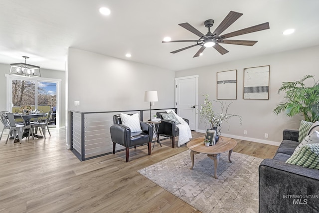 living area with light wood-style floors, recessed lighting, baseboards, and ceiling fan with notable chandelier