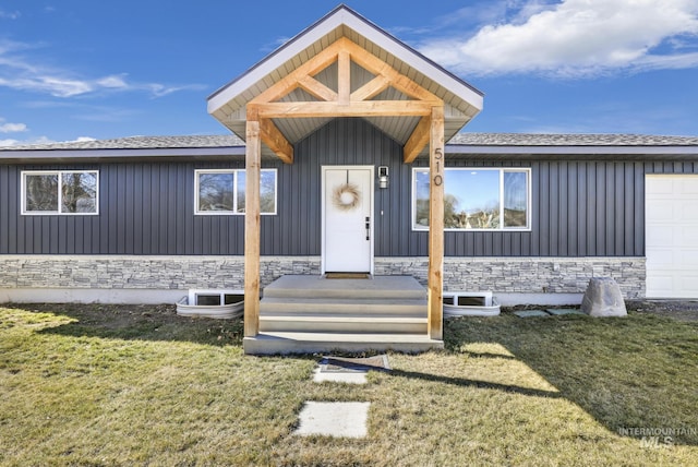 entrance to property featuring an attached garage, stone siding, board and batten siding, and a lawn