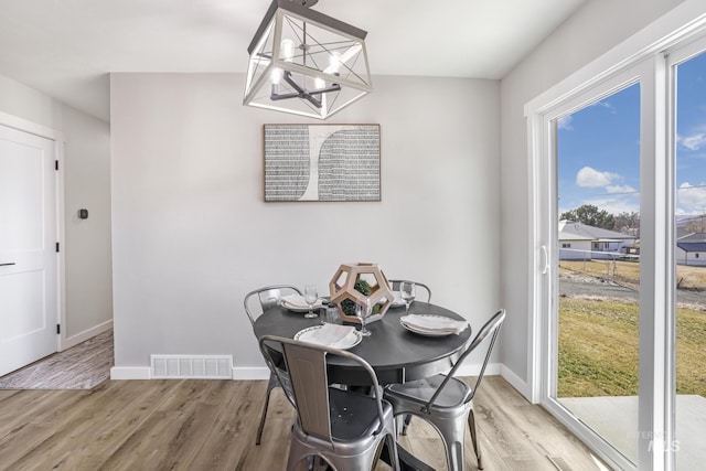 dining space featuring light wood-type flooring, visible vents, baseboards, and an inviting chandelier