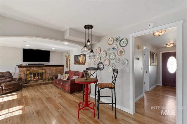 living area featuring a brick fireplace, light wood-style flooring, and baseboards