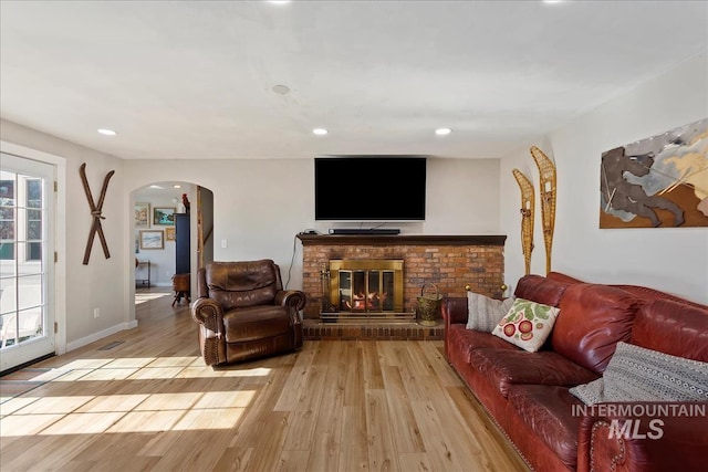 living area featuring a wealth of natural light, arched walkways, a brick fireplace, and light wood-style flooring