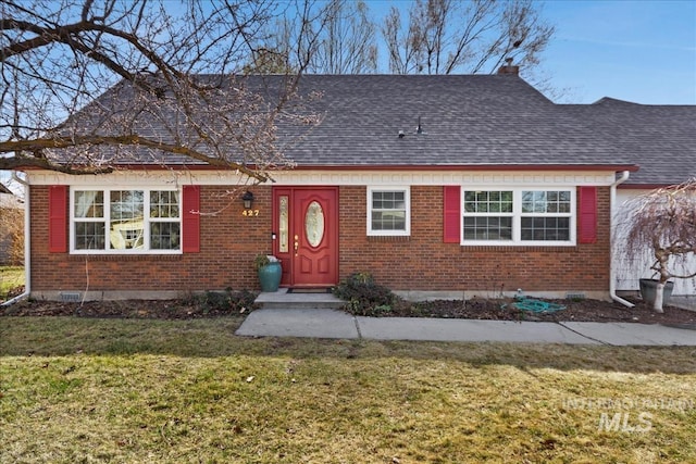 view of front facade featuring brick siding, a chimney, a front yard, and a shingled roof