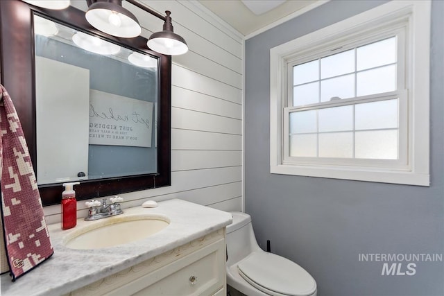 bathroom featuring toilet, vanity, wood walls, and ornamental molding