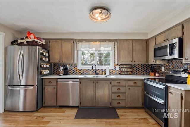 kitchen with light wood finished floors, a sink, light countertops, appliances with stainless steel finishes, and tasteful backsplash