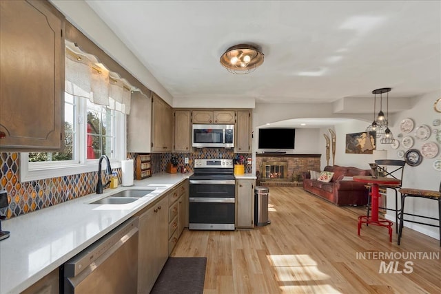 kitchen with a sink, backsplash, appliances with stainless steel finishes, light countertops, and a brick fireplace