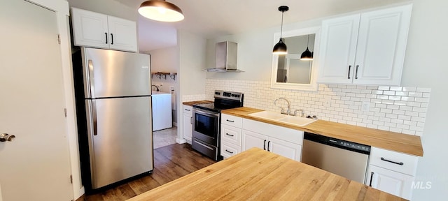 kitchen featuring appliances with stainless steel finishes, wall chimney exhaust hood, white cabinets, decorative light fixtures, and butcher block counters