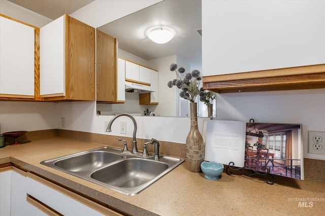 kitchen with a sink, under cabinet range hood, and white cabinetry